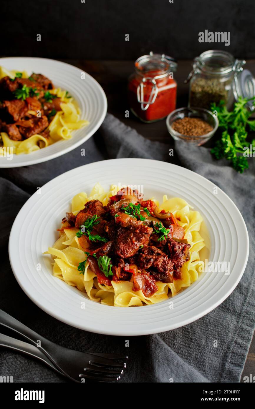 Goulash allemand servi sur des nouilles aux œufs dans des bols peu profonds : morceaux de bœuf mijotés assaisonnés de marjolaine, de graines de carvi et de paprika Banque D'Images