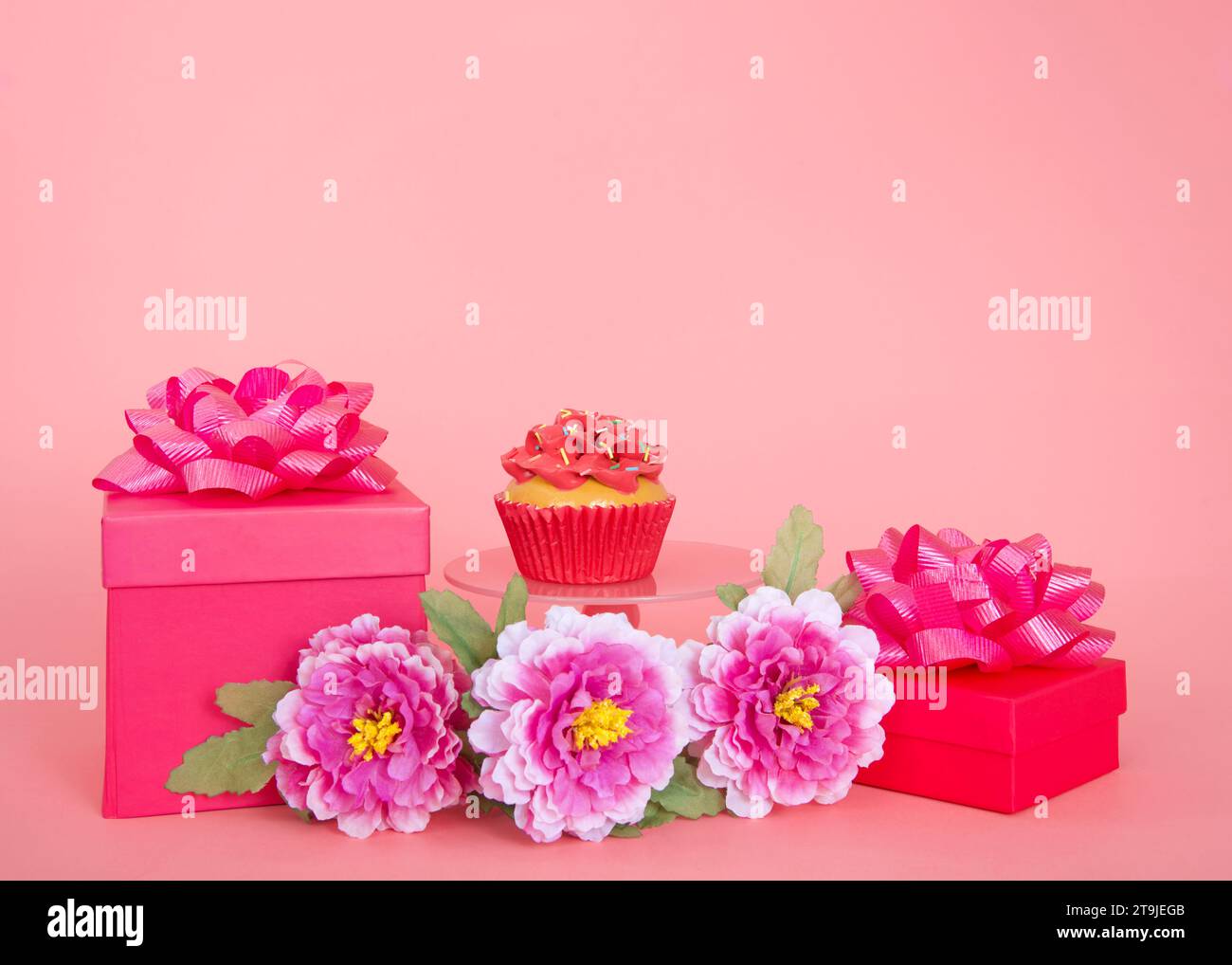 Cupcake à la fraise unique sur piédestal rose avec des cadeaux et des fleurs rose vif. Sur un fond rose avec espace de copie. Banque D'Images