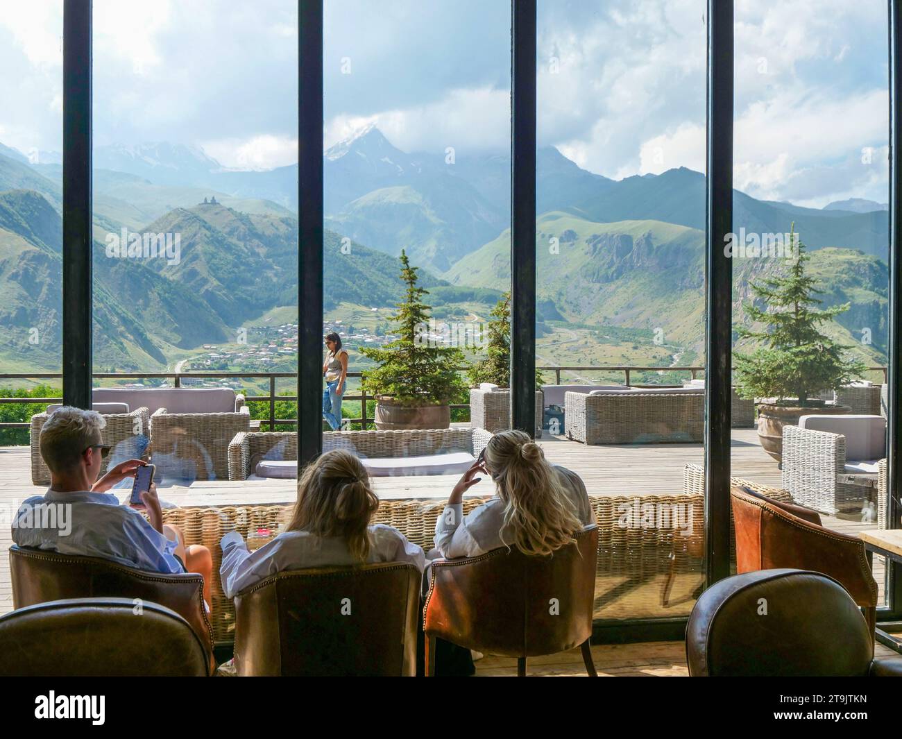 Les gens boivent du café et se détendent avec une vue imprenable sur les montagnes du Caucase, le mont Kazbek et Gergeti Trinity Church à travers les fenêtres du café. Été. Banque D'Images