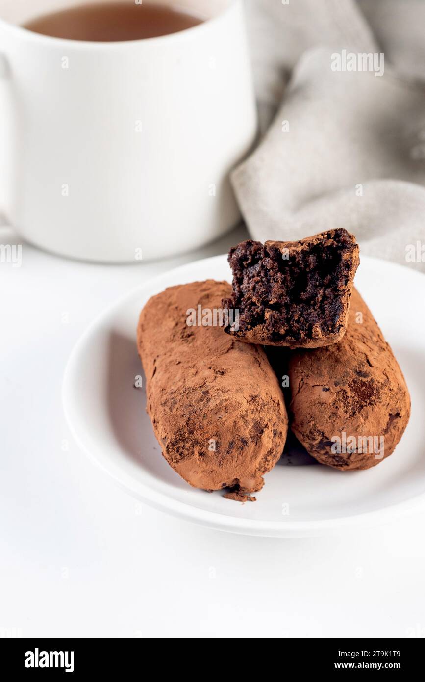 Gâteau aux pommes de terre au chocolat. biscuit avec crème et poudre de cacao sur plaque. Dessert à la truffe, saupoudré de poudre de cacao, et tasse de thé sur la table blanche. Banque D'Images