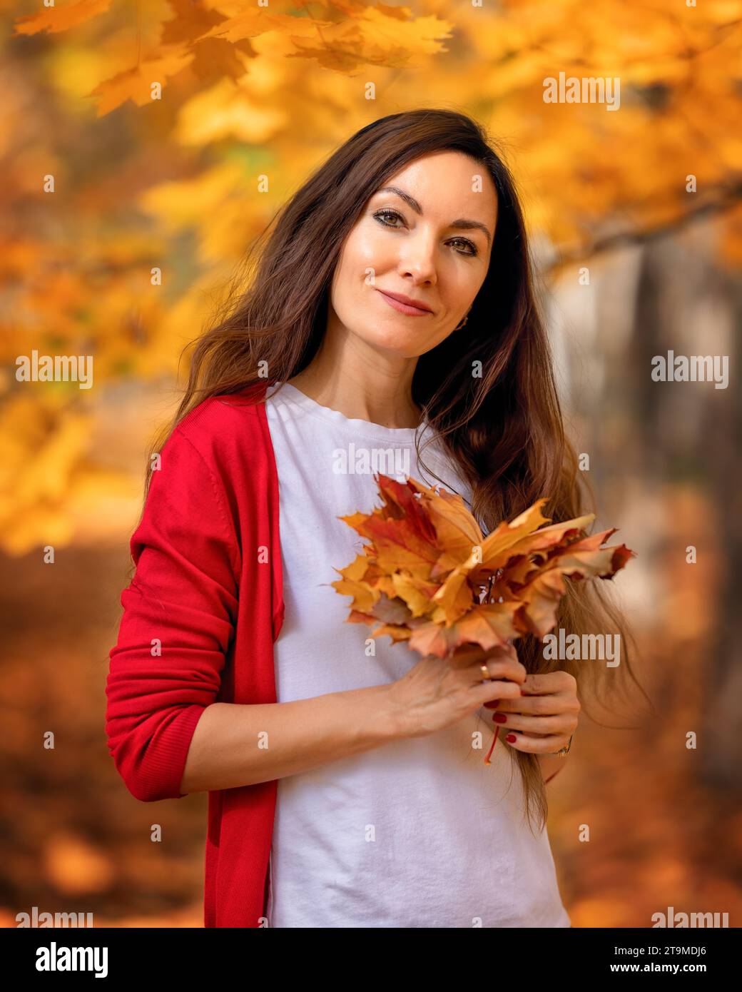 Portrait de femme heureuse avec les cheveux longs jouant avec les feuilles jaunes d'automne dans le parc pendant l'automne en plein air. Automne chaud Banque D'Images