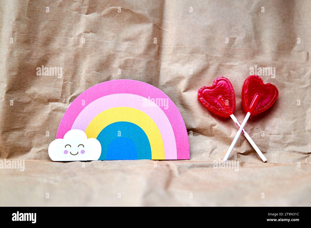 Deux sucettes rouges en forme de coeur avec une carte en forme d'arc-en-ciel sur un fond en carton. Banque D'Images