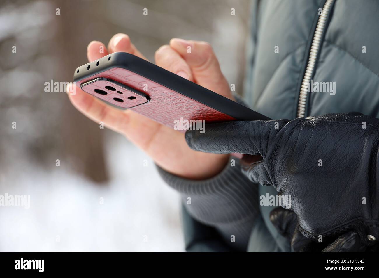 Les mains des femmes avec smartphone se rapprochent sur un arrière-plan flou. Femme utilisant un téléphone portable se tient dans une rue dans la neige hiver Banque D'Images
