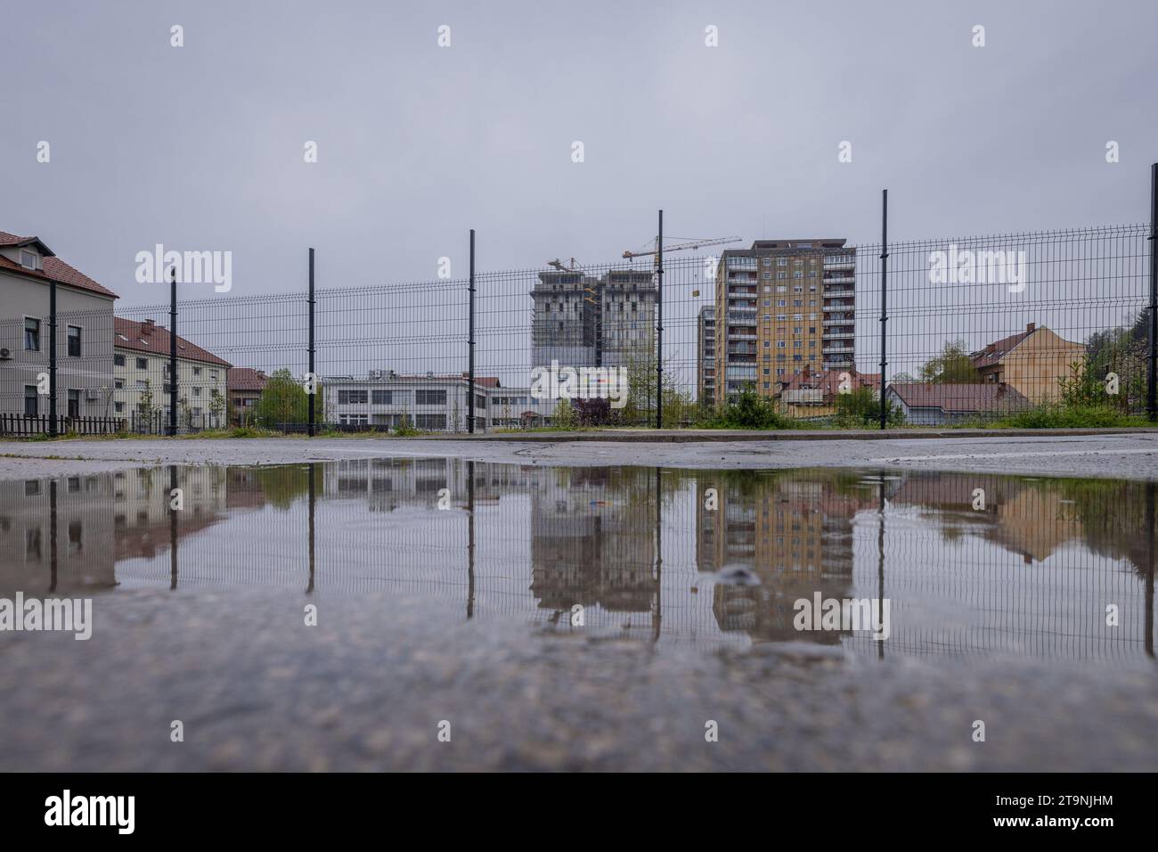 Maisons modernes en construction, reflet visible dans la flaque d'eau au sol, clôture au premier plan. concept de construction interdite ou sans permis. Banque D'Images