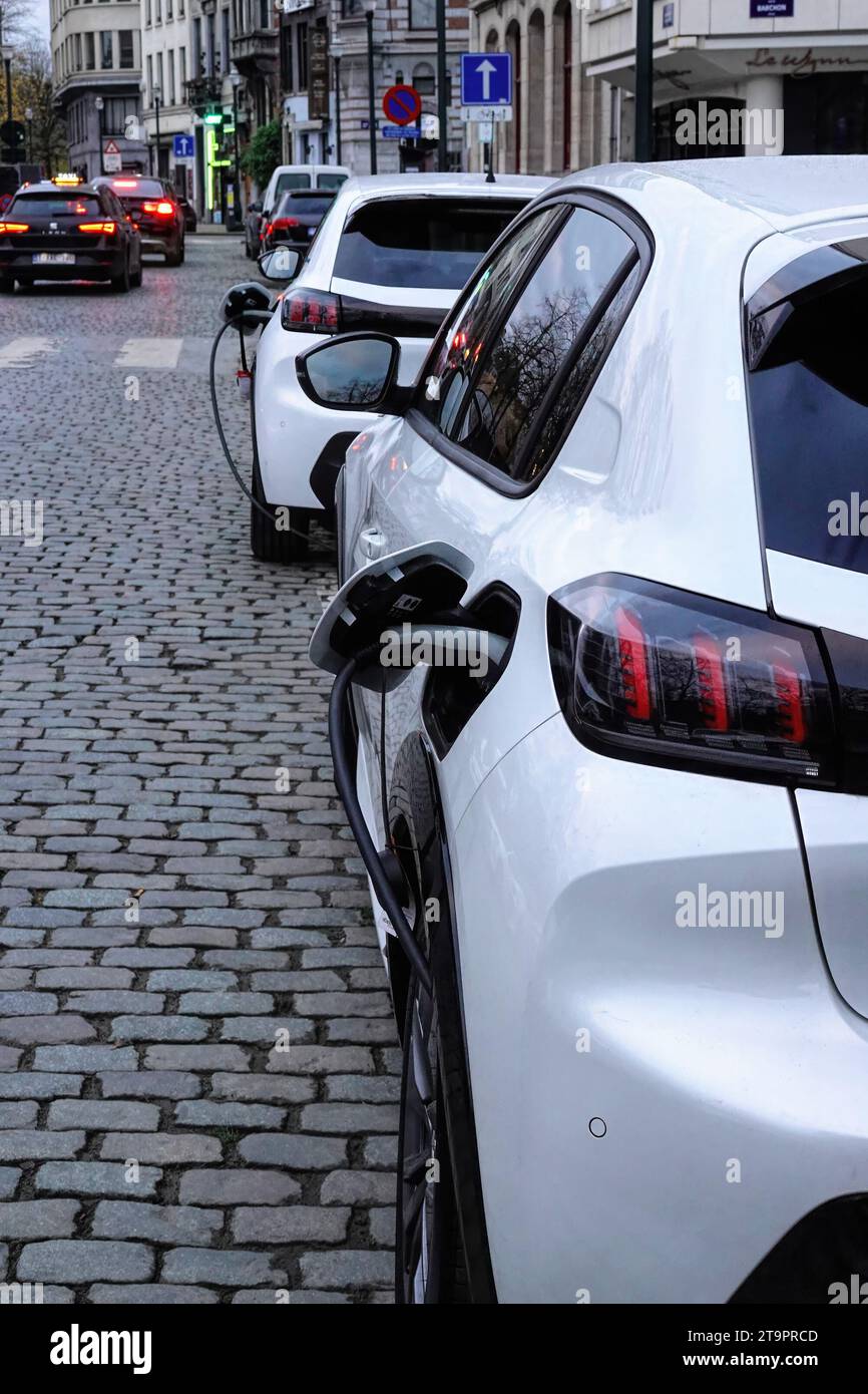 Gros plan vertical sur un 2 voitures électriques blanches en charge dans les rues en pierre coble de Bruxelles Banque D'Images