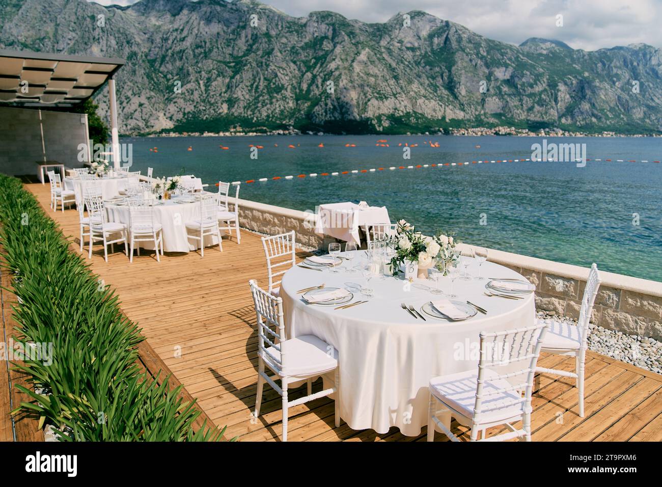 Tables rondes disposées sur une terrasse en bois dans un jardin surplombant la mer Banque D'Images