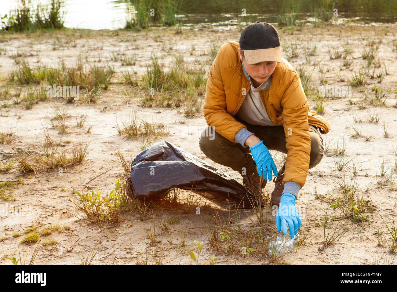 Cette photographie représente un individu engagé dans un nettoyage environnemental, ramassant des déchets sur une plage sablonneuse. Vêtue d’une veste et d’un bonnet décontractés, la personne est munie de gants et d’un sac poubelle, témoignage de son engagement à préserver les espaces naturels. Leur attitude ciblée souligne l'importance de l'action individuelle dans la lutte contre les problèmes environnementaux tels que la pollution et la conservation des habitats. Soin conscient : effort de nettoyage de la plage. Photo de haute qualité Banque D'Images