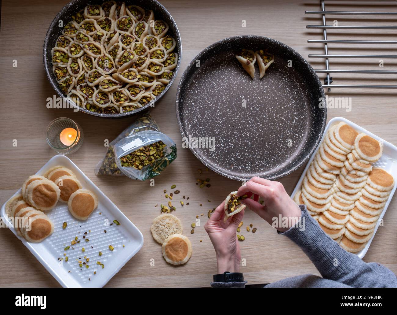 Mains tenant Qatayef rempli de chocolat et garni de pistaches sur une table en bois, avec une assiette à préparer au four plus tard comme Ramadan swe Banque D'Images