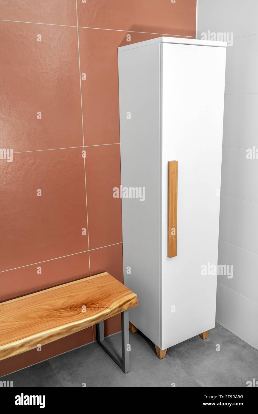 Banc en bois Live Edge avec pieds en métal gris et armoire blanche avec poignées et pieds en bois dans la salle de bains Banque D'Images