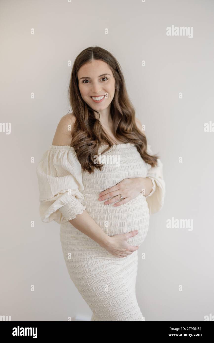 Portrait de femme enceinte en robe de maternité blanche embrassant le ventre Banque D'Images
