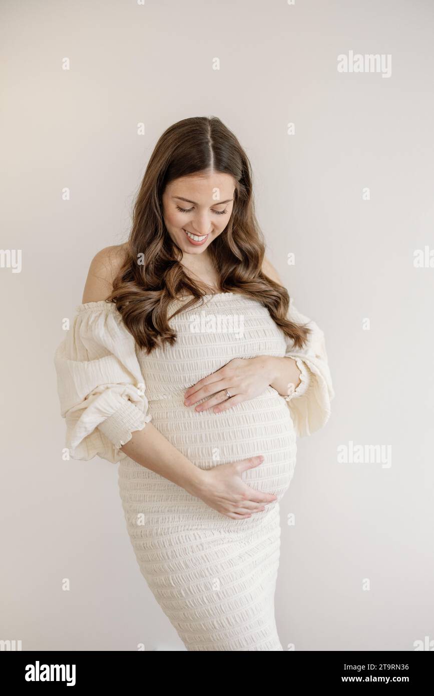 Portrait de femme enceinte en robe de maternité blanche admirant le ventre Banque D'Images