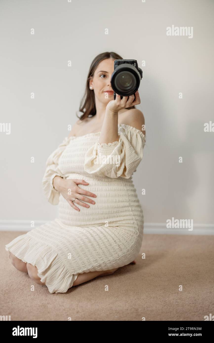 Autoportrait d'une femme enceinte agenouillée sur le sol en robe de maternité Banque D'Images