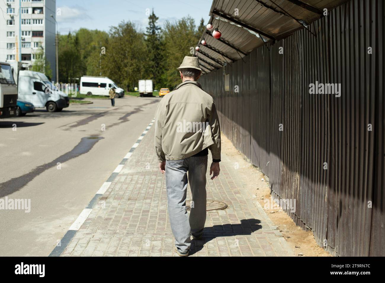 Le gars marche dans la rue le long de la clôture. Homme en été en ville. Banque D'Images