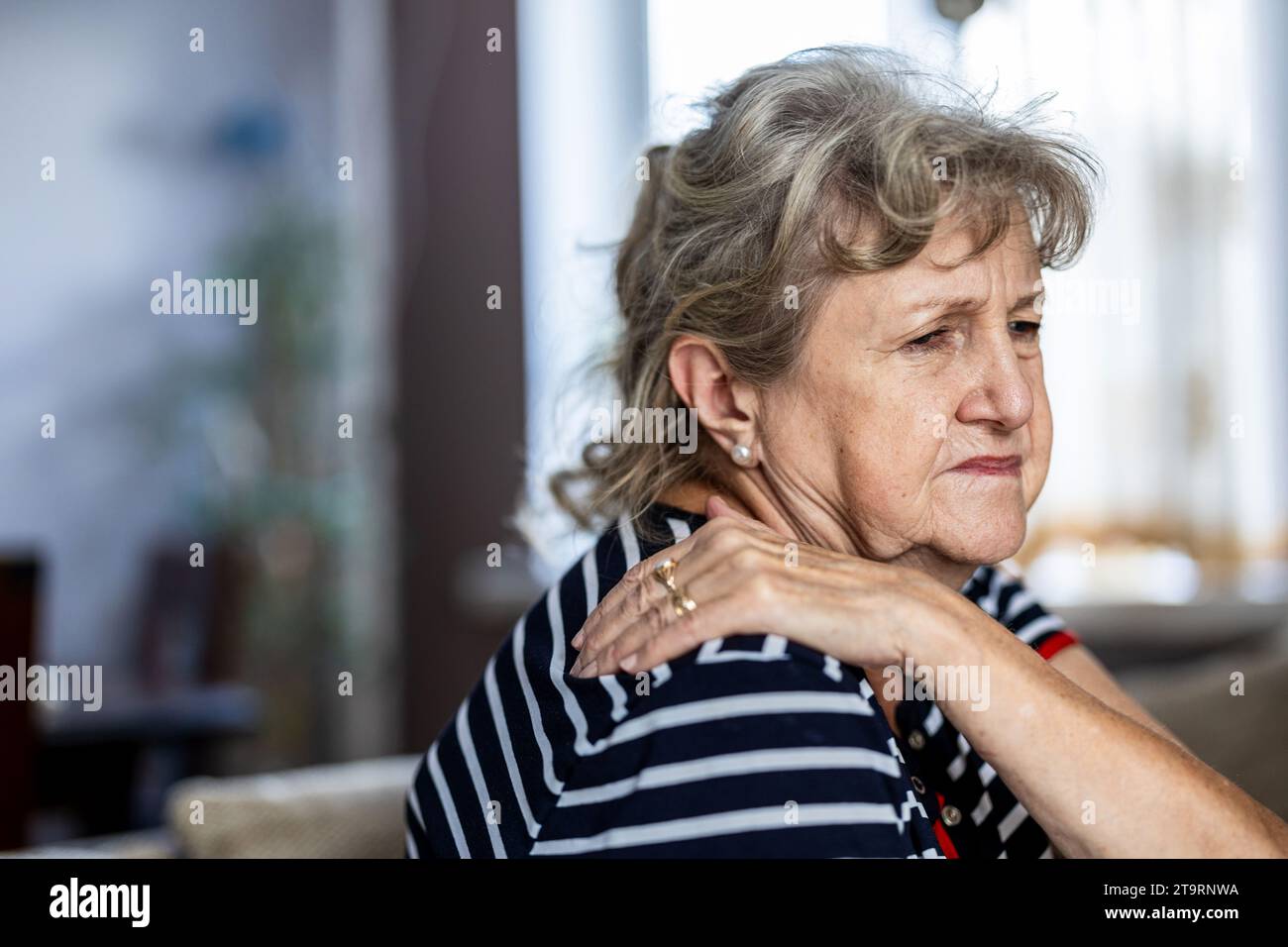 Portrait d'une femme âgée souffrant de douleurs au cou alors qu'elle était assise sur un canapé à la maison Banque D'Images