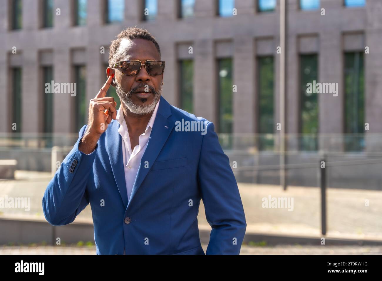Cool mature homme d'affaires africain portant des lunettes de soleil et costume utilisant des écouteurs pour parler au mobile à l'extérieur Banque D'Images