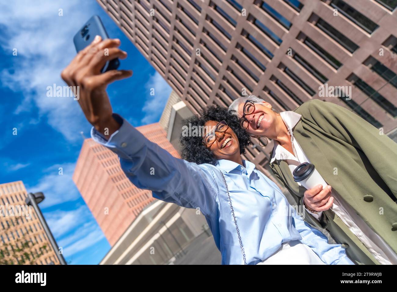 Photo dynamique à faible angle de vue de femmes d'affaires multiculturelles prenant un selfie souriant à la caméra à l'extérieur Banque D'Images