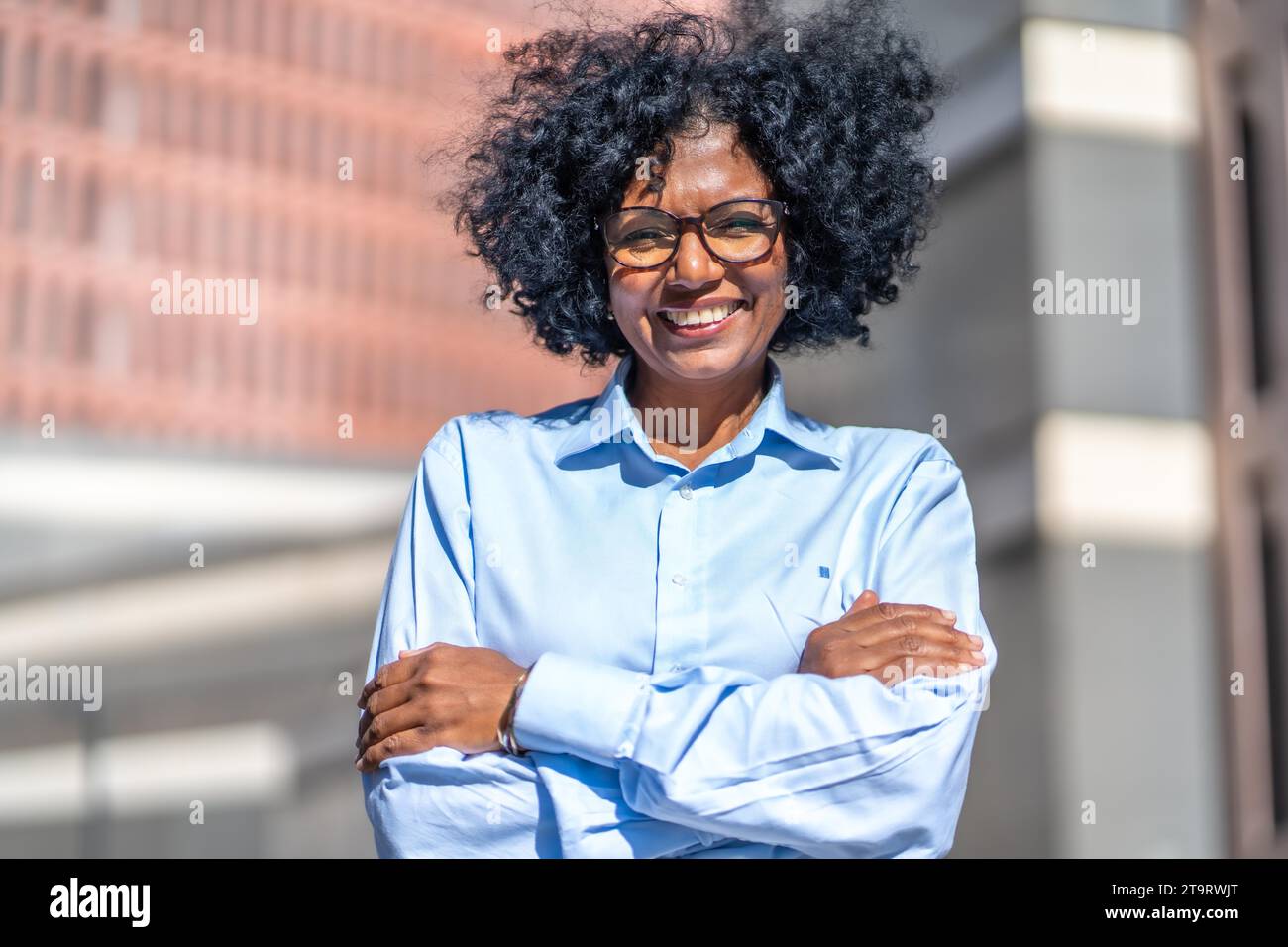 Portrait d'une femme d'affaires africaine souriante et fière avec les bras croisés à l'extérieur d'un bâtiment financier Banque D'Images