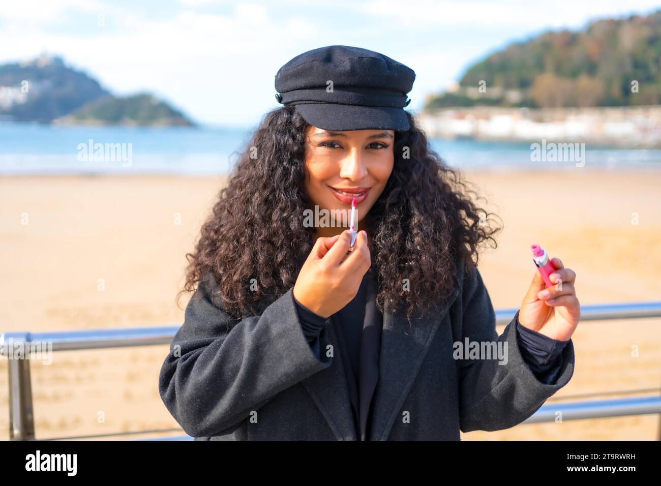 Femme latine se maquillant avec du rouge à lèvres à côté de la plage pendant une journée ensoleillée en hiver Banque D'Images