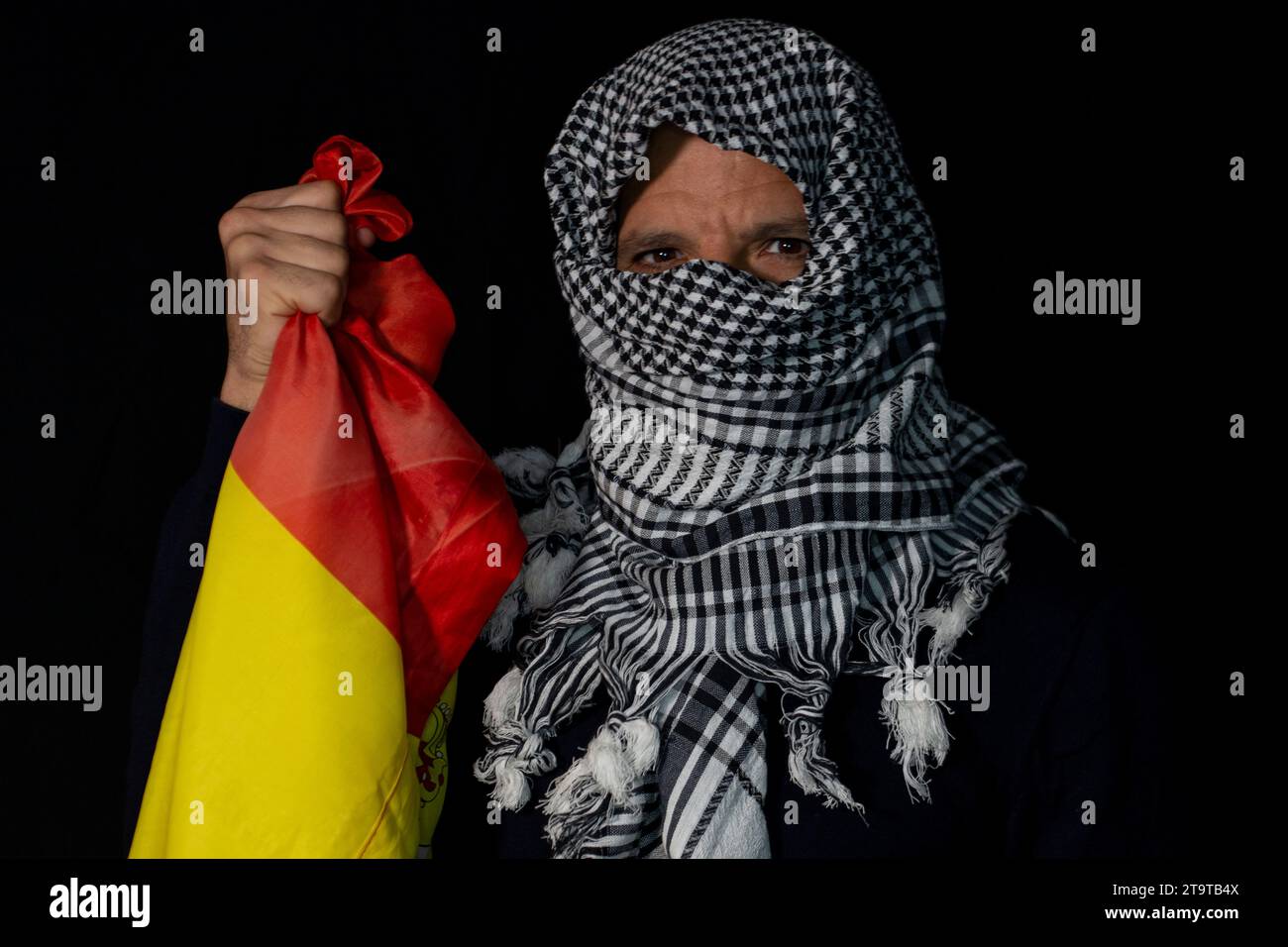 Homme adulte avec une écharpe palestinienne mis sur sa tête sur un fond noir tenant un drapeau de l'Espagne Banque D'Images