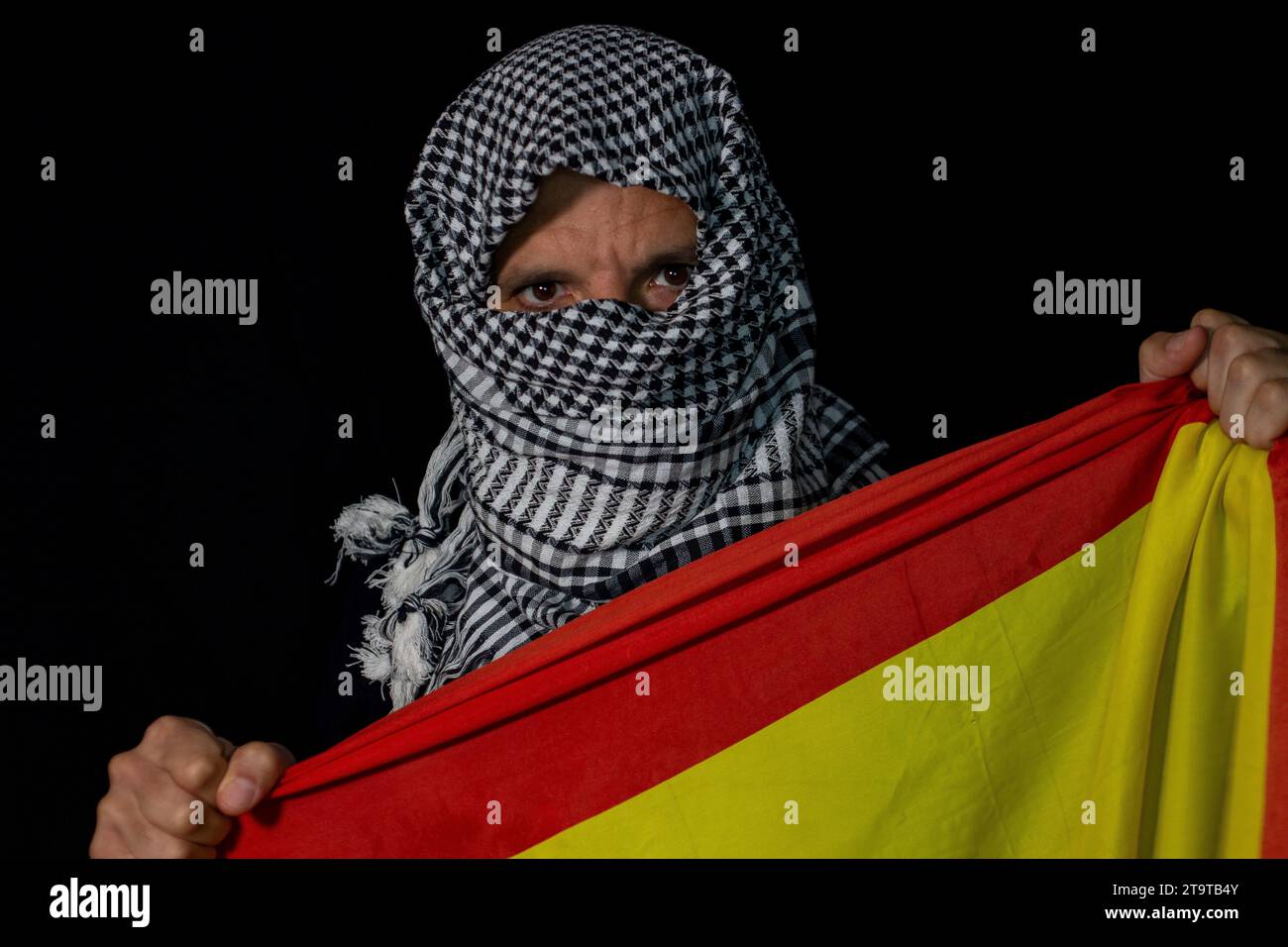 Homme adulte avec une écharpe palestinienne mis sur sa tête sur un fond noir tenant un drapeau de l'Espagne Banque D'Images