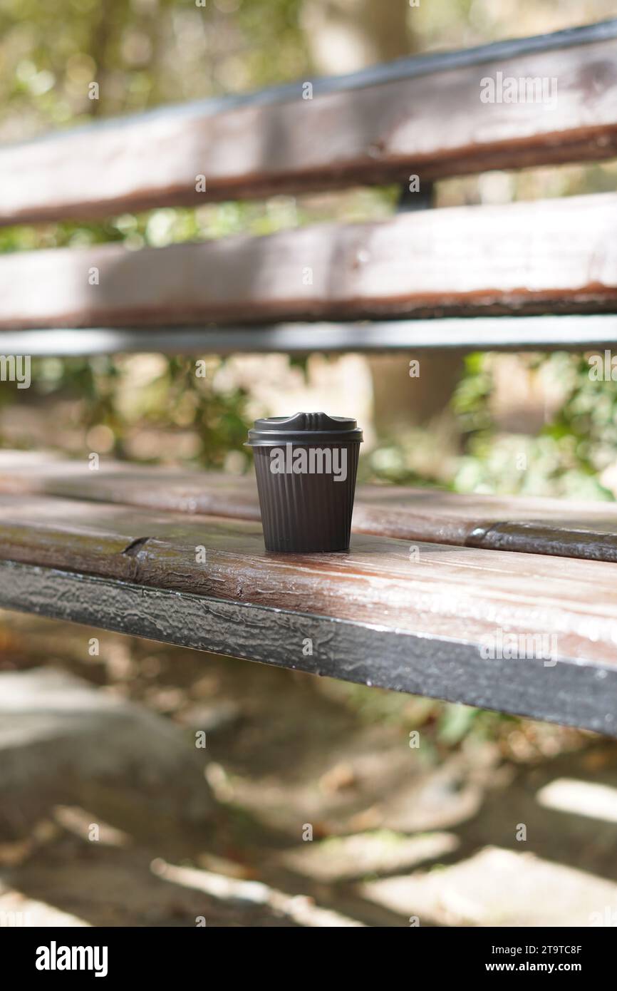 Une tasse à café en papier assise sur un banc de parc. Banque D'Images