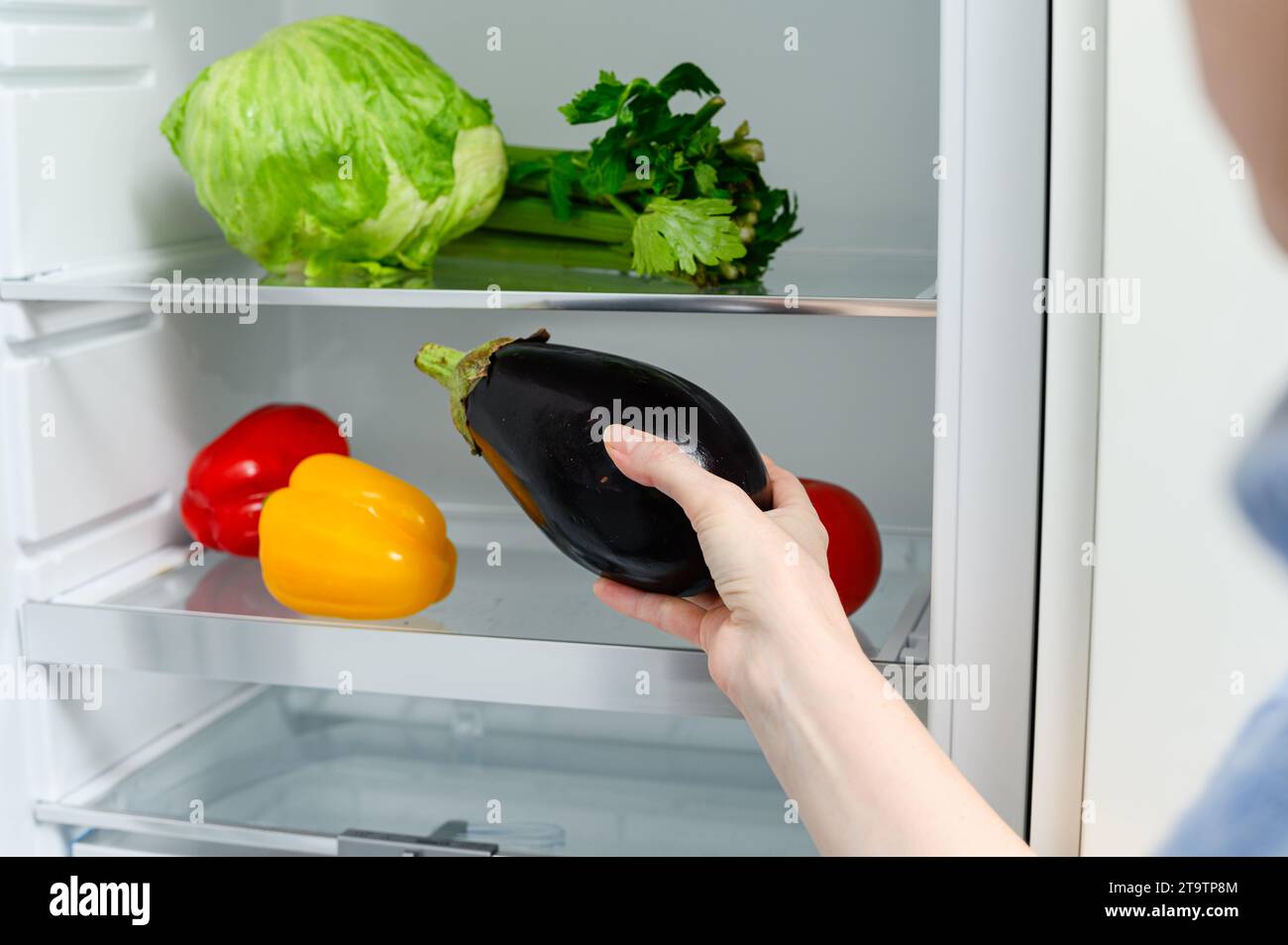 Une femme met une aubergine dans le réfrigérateur. Légumes frais couchés sur la clayette du réfrigérateur. Banque D'Images