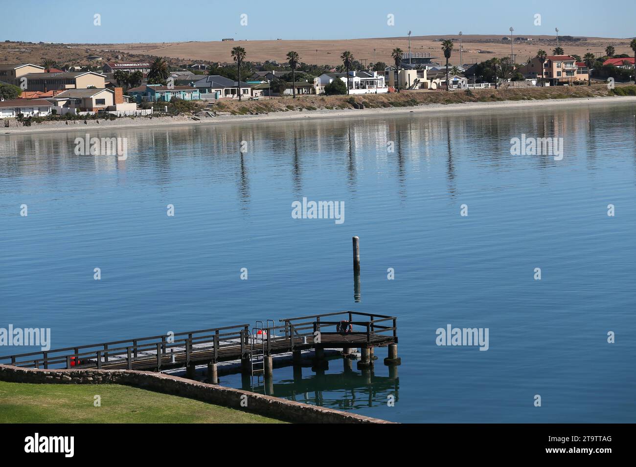 Une vue générale d'une jetée en bois et de l'eau calme avec une plage et des maisons en arrière-plan. Banque D'Images