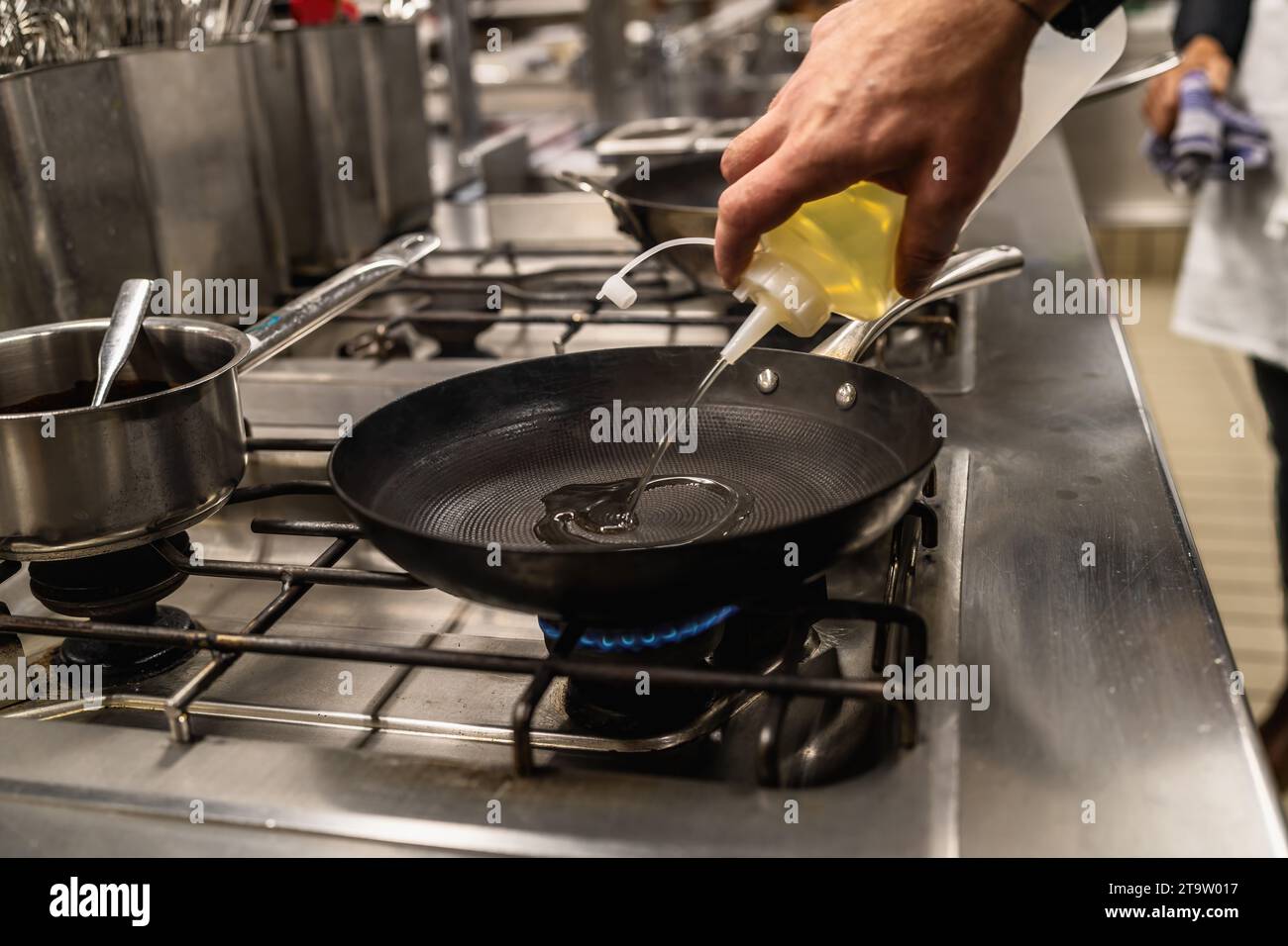 Chef cuisinier verser l'huile dans une poêle chauffée. Image concept de cuisine d'hôtel de luxe. Banque D'Images