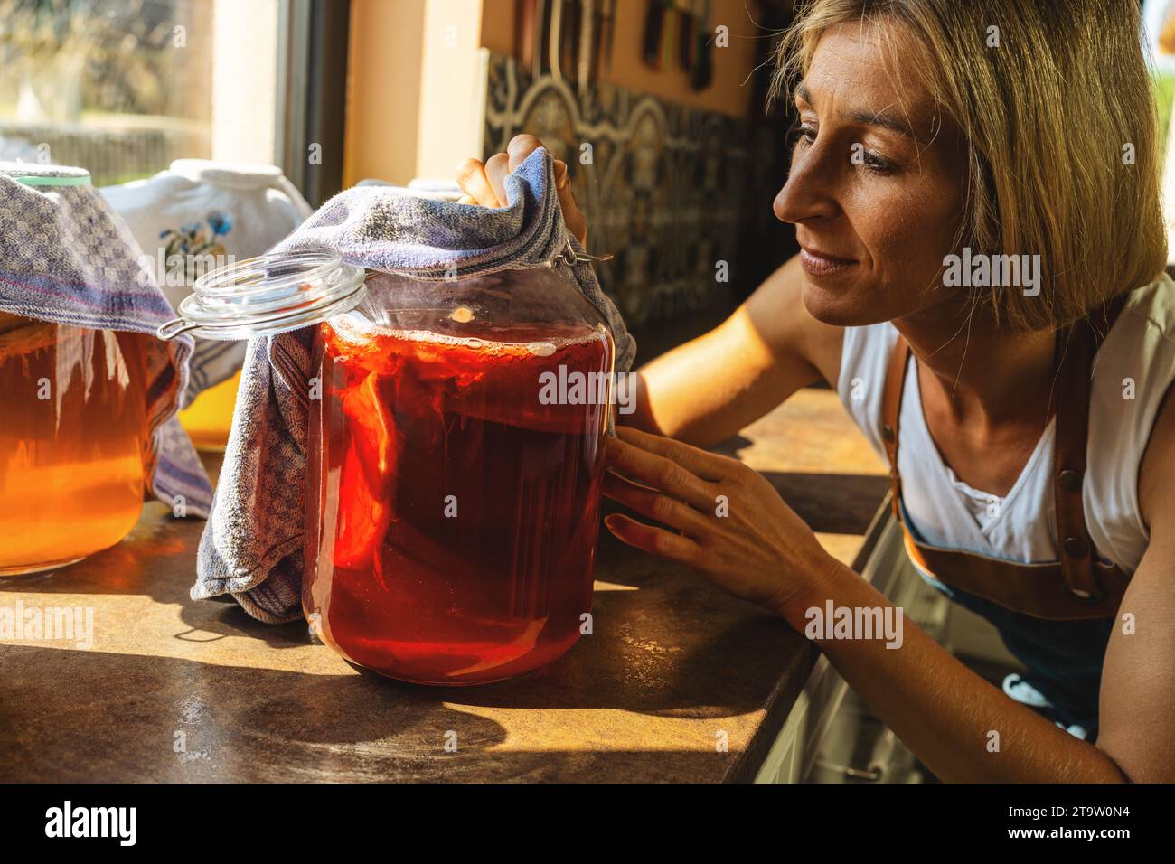 Une femme heureuse a examiné le tee-shirt kombucha avec des couches de champignons dans un grand bocal. Aliments fermentés de boisson saine biologique, boisson nutritive probiotique pour un bon balanc Banque D'Images