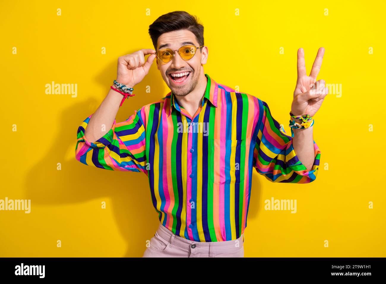 Portrait de jeune homme faisant la promotion de tenues vintage dans son magasin d'occasion touchant Sunglass show v signe isolé sur fond de couleur jaune Banque D'Images