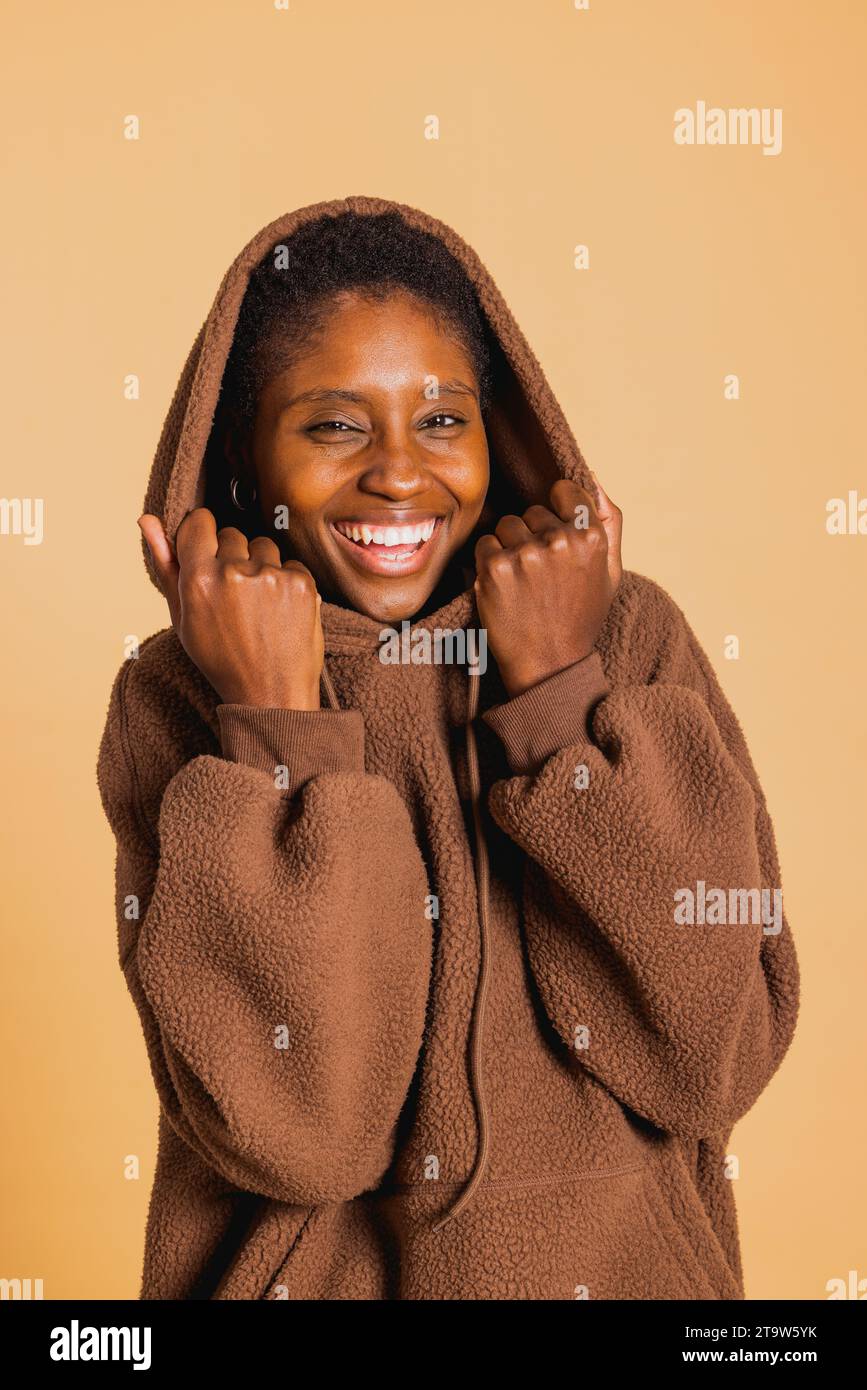 Portrait de jeune femme afro-américaine joyeuse portant un pull à capuche marron sur fond marron Banque D'Images