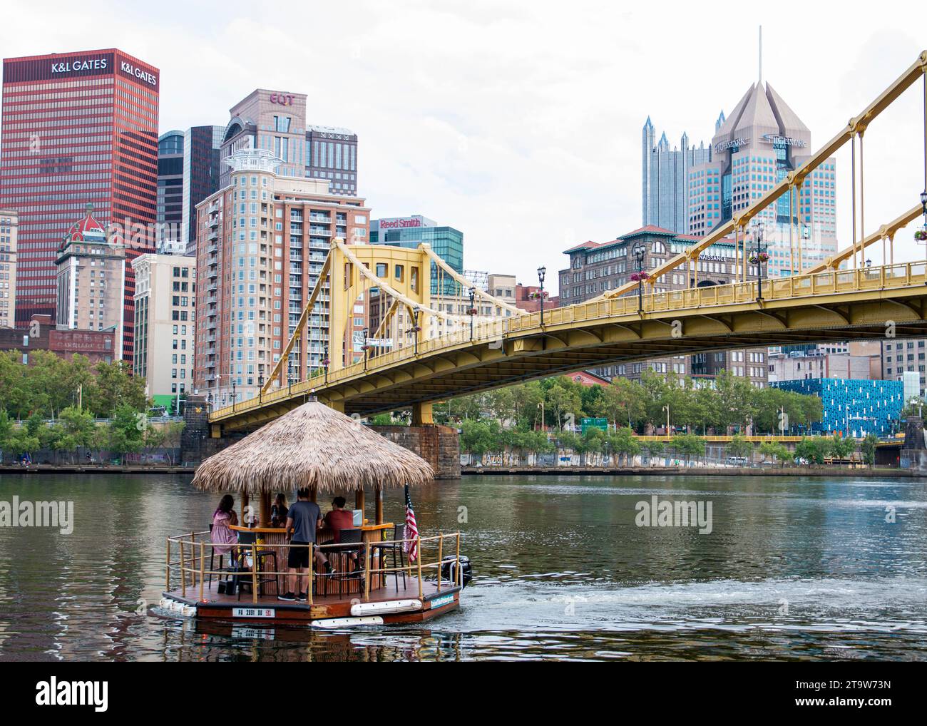 Pittsburgh, Pennsylvanie, États-Unis - 6 août 2023 : un bar flottant de bateau Tiki avec un toit de chaume sur une rivière avec un pont en arrière-plan sur l'Allegan Banque D'Images