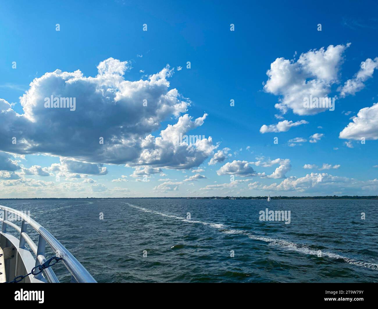 Un bateau voyageant à travers un grand plan d'eau avec des nuages gonflés bas et un ciel bleu. Banque D'Images