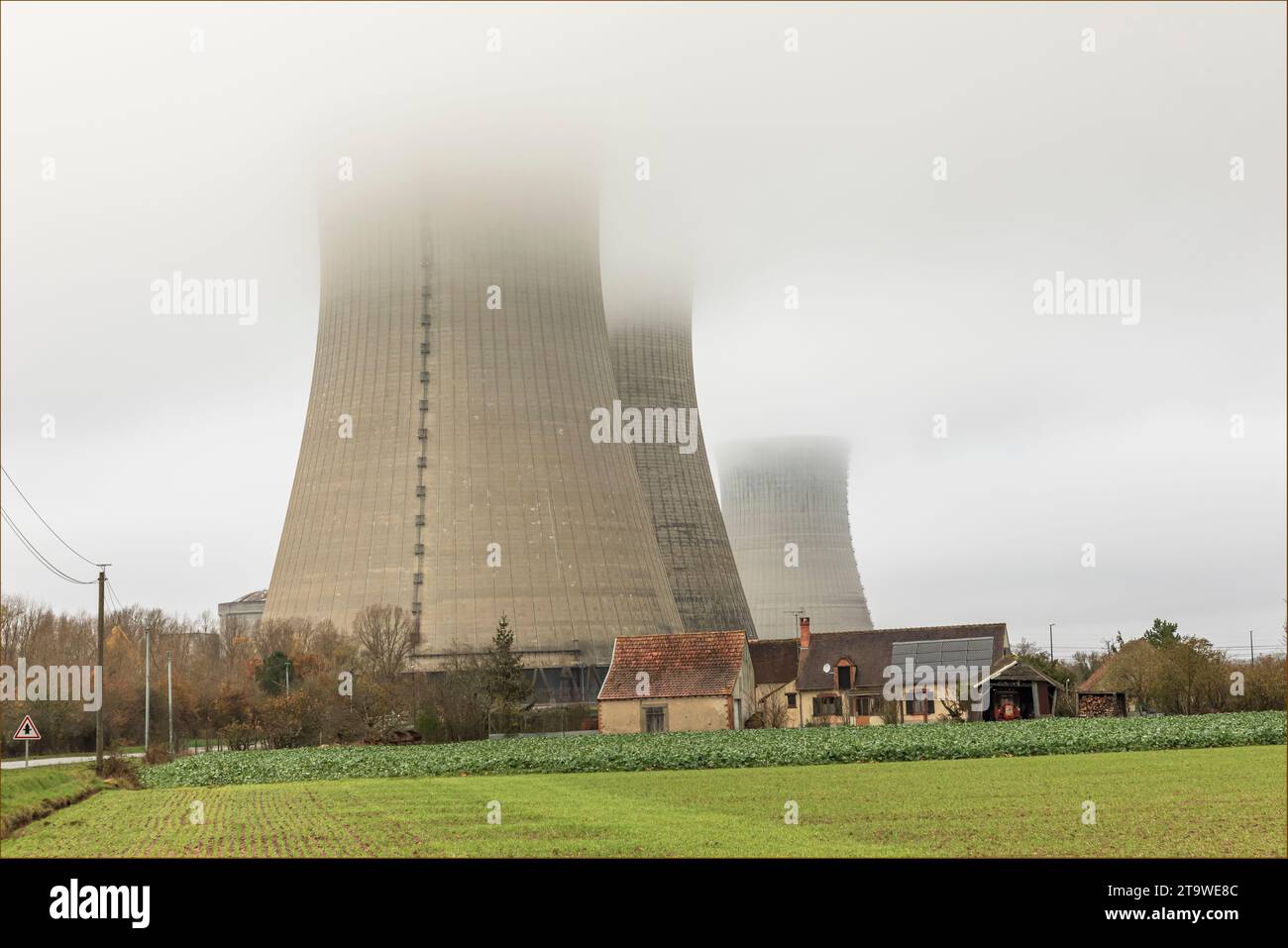 Ancienne ferme française sous les tours de refroidissement de la centrale nucléaire un jour où il y a des nuages bas Banque D'Images