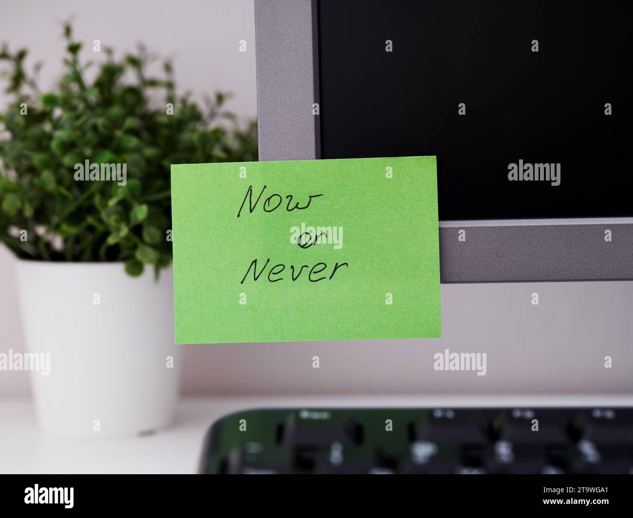 Un papier vert avec le rappel maintenant ou jamais dessus collé sur un moniteur dans un lieu de travail de bureau. Banque D'Images