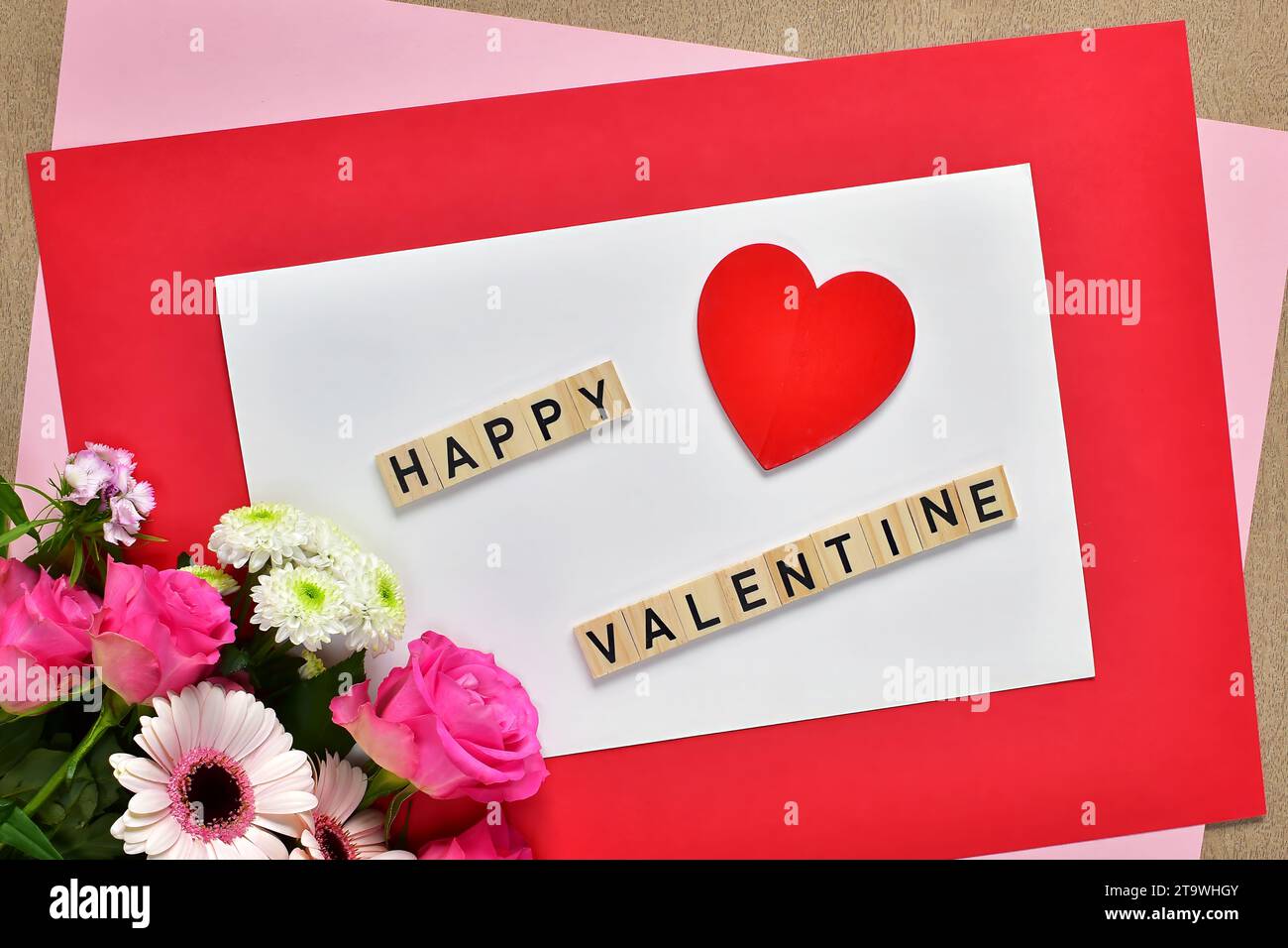 Carte de voeux de Saint-Valentin. Coeur rouge, bouquet de fleurs roses et lettres Happy Valentine sur fond de papier blanc, composition de pose plate. Banque D'Images