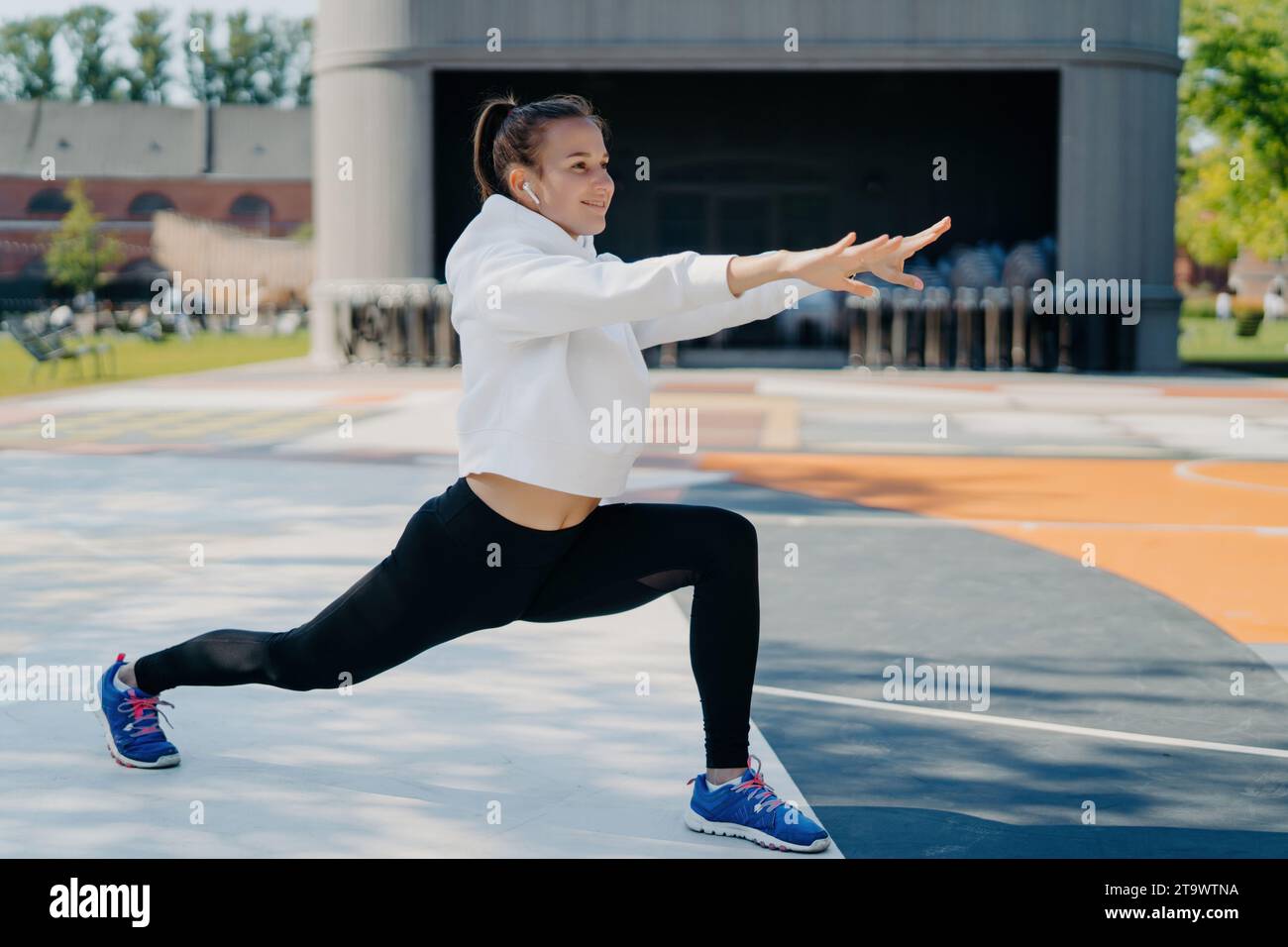 Femme souriante faisant des fentes à l'extérieur, profitant d'une séance d'entraînement dans le parc Banque D'Images
