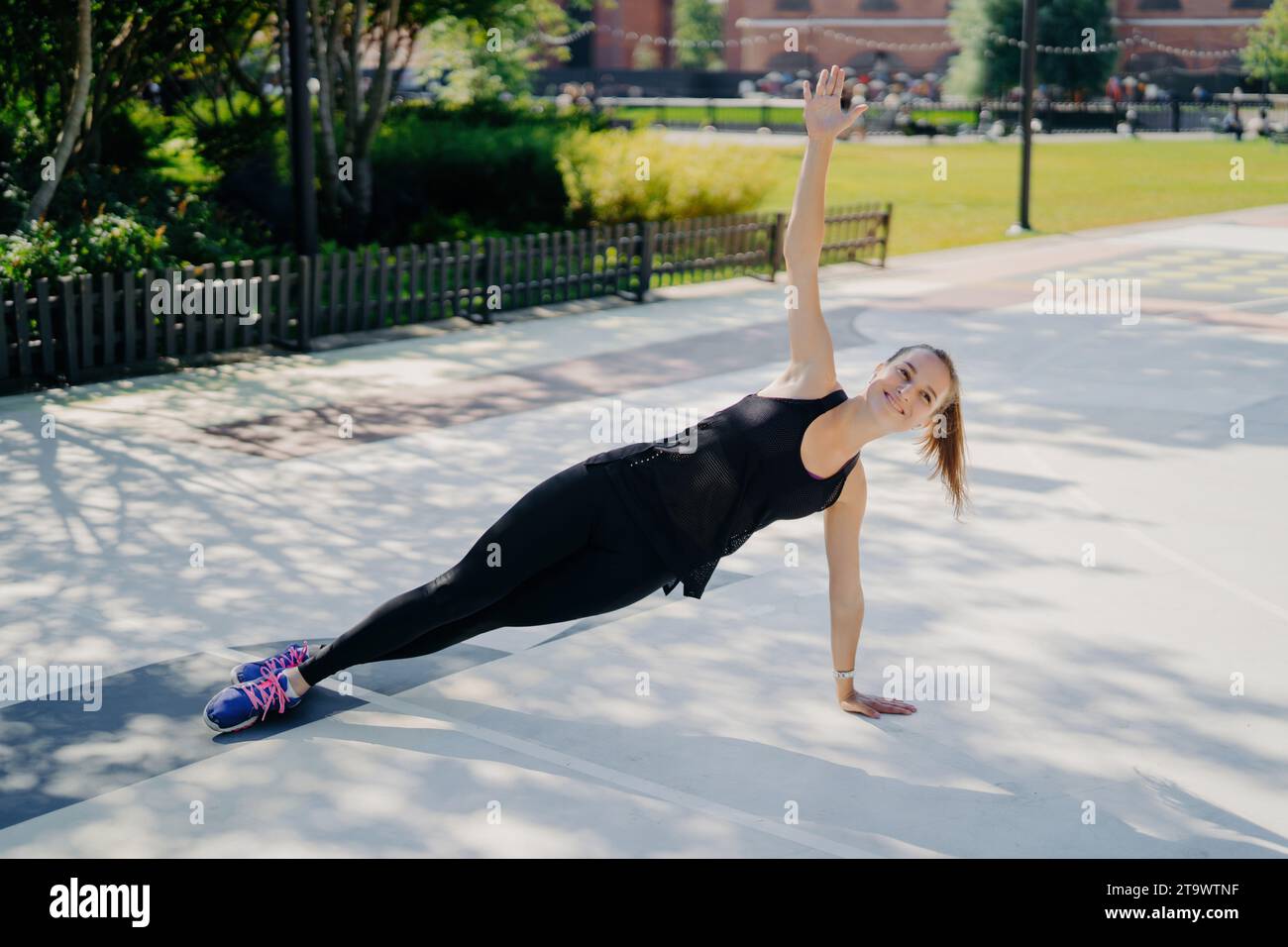 Femme joyeuse exécutant la planche latérale dans le parc ensoleillé, favorisant le bien-être Banque D'Images