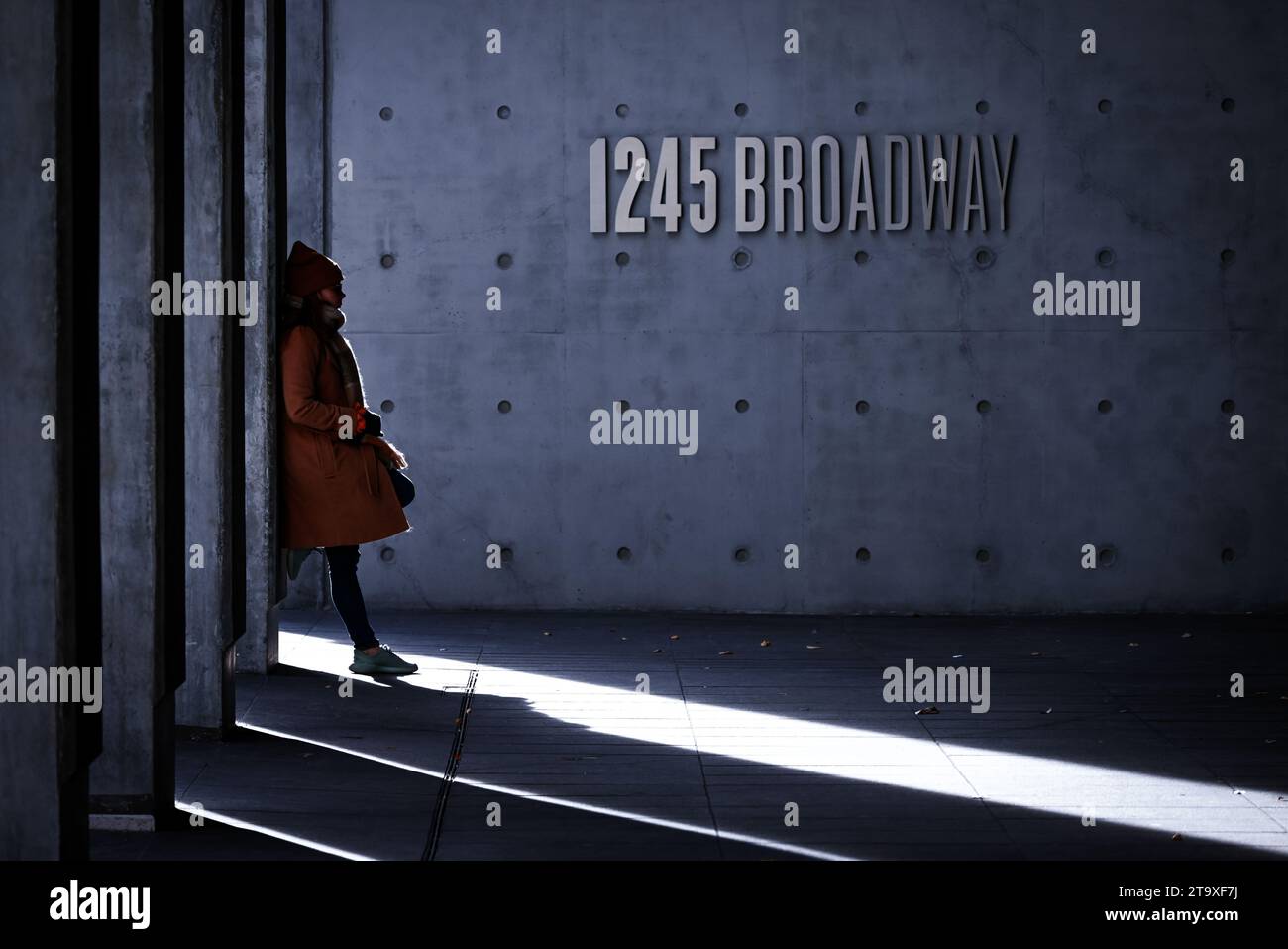 Femme en manteau d'hiver et bonnet penché avec désinvolture contre l'immeuble de bureaux sur Broadway New York City, New York Banque D'Images