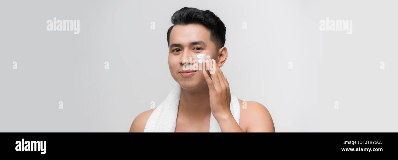 Jeune homme asiatique applique une crème hydratante sur son visage. Soins de la peau masculine. Banque D'Images