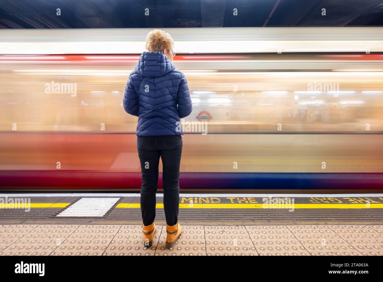 Un voyageur se tenant sur le quai de la station de métro Monument sur le métro londonien alors qu'un train de métro passe à travers la gare Banque D'Images
