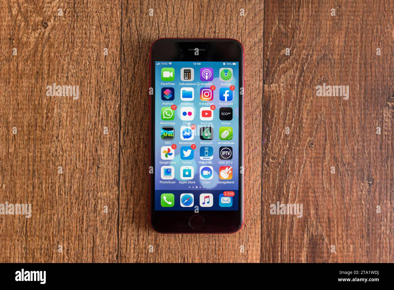 Apple iPhone se second Edition 'Product Red' allumé et affichant des icônes sur un fond en bois. Banque D'Images