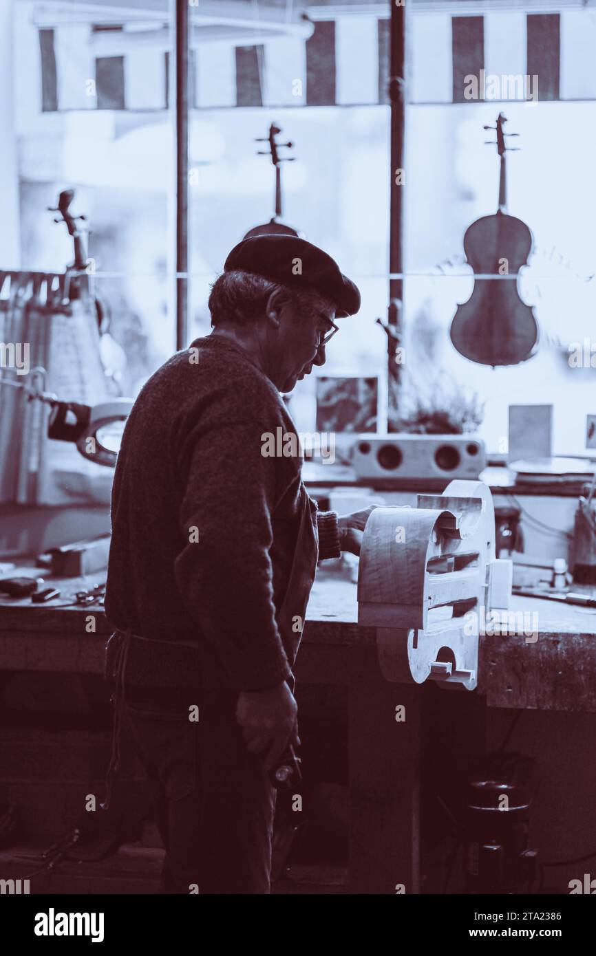Expert senior luthier artisan violoniste sculpter les côtes ciselées d'un nouveau modèle classique violoncelle dans l'atelier Crémone Italie, monochrome Banque D'Images
