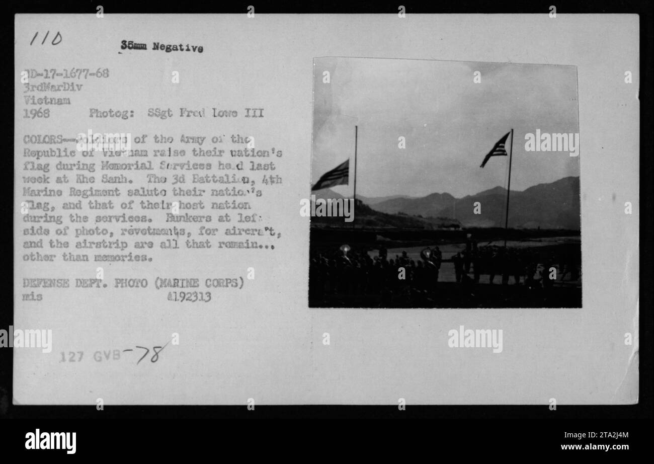 Pendant les services commémoratifs de 1968 à Khe Sanh, les soldats de l'armée de la République du Vietnam lèvent leur drapeau tandis que le 3e bataillon, le 4e régiment de Marines salue ; les bunkers, les revêtements et la piste d'atterrissage sont visibles. Banque D'Images