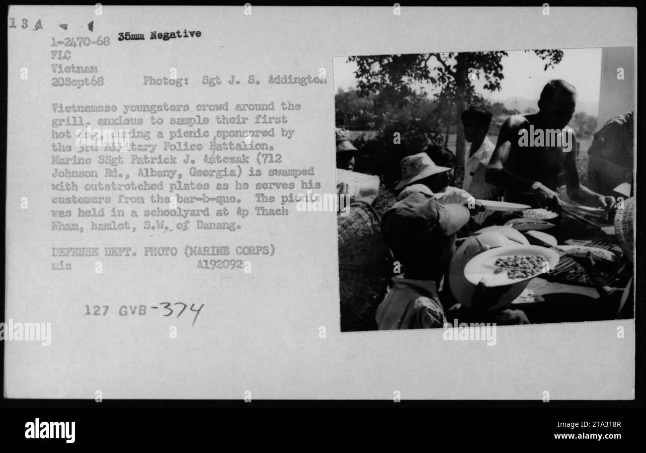 Les enfants vietnamiens attendent avec impatience leur premier goût d’un hot dog lors d’un pique-nique organisé par le 3e bataillon de la police militaire. Le sergent d'état-major Patrick J. Tezak, stationné à Albany, en Géorgie, a servi les enfants alors qu'ils se tendaient autour de lui avec des plaques tendues à la cour d'école AP Thach Nham, au sud-ouest de Danang. Cet événement a été documenté le 20 septembre 1968. Photographie prise par le Sgt J. S. Addington. Banque D'Images