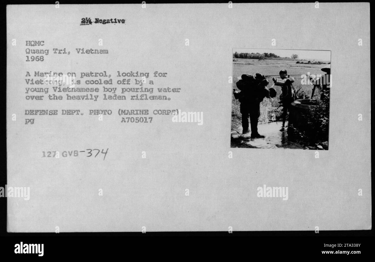 Un Marine en patrouille à Quang Tri, Vietnam en 1968 est refroidi par un jeune garçon vietnamien versant de l'eau sur le fusil lourdement chargé du Marine. Cette photographie, prise pendant la guerre du Vietnam, capture un moment d'interaction entre l'armée américaine et la population civile vietnamienne locale. Banque D'Images