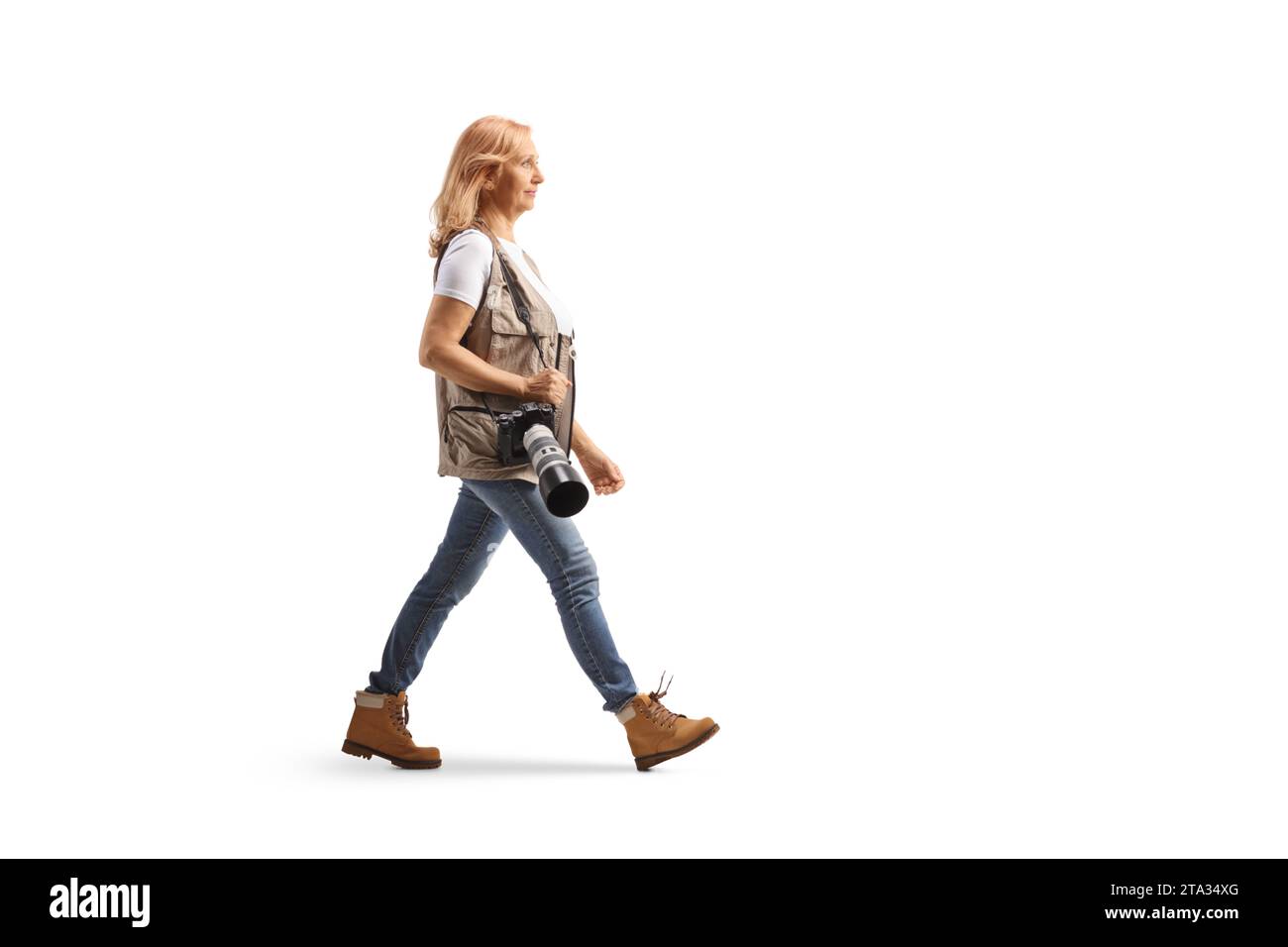 Photo de profil pleine longueur d'une photographe femme marchant avec un appareil photo sur une bandoulière isolée sur fond blanc Banque D'Images