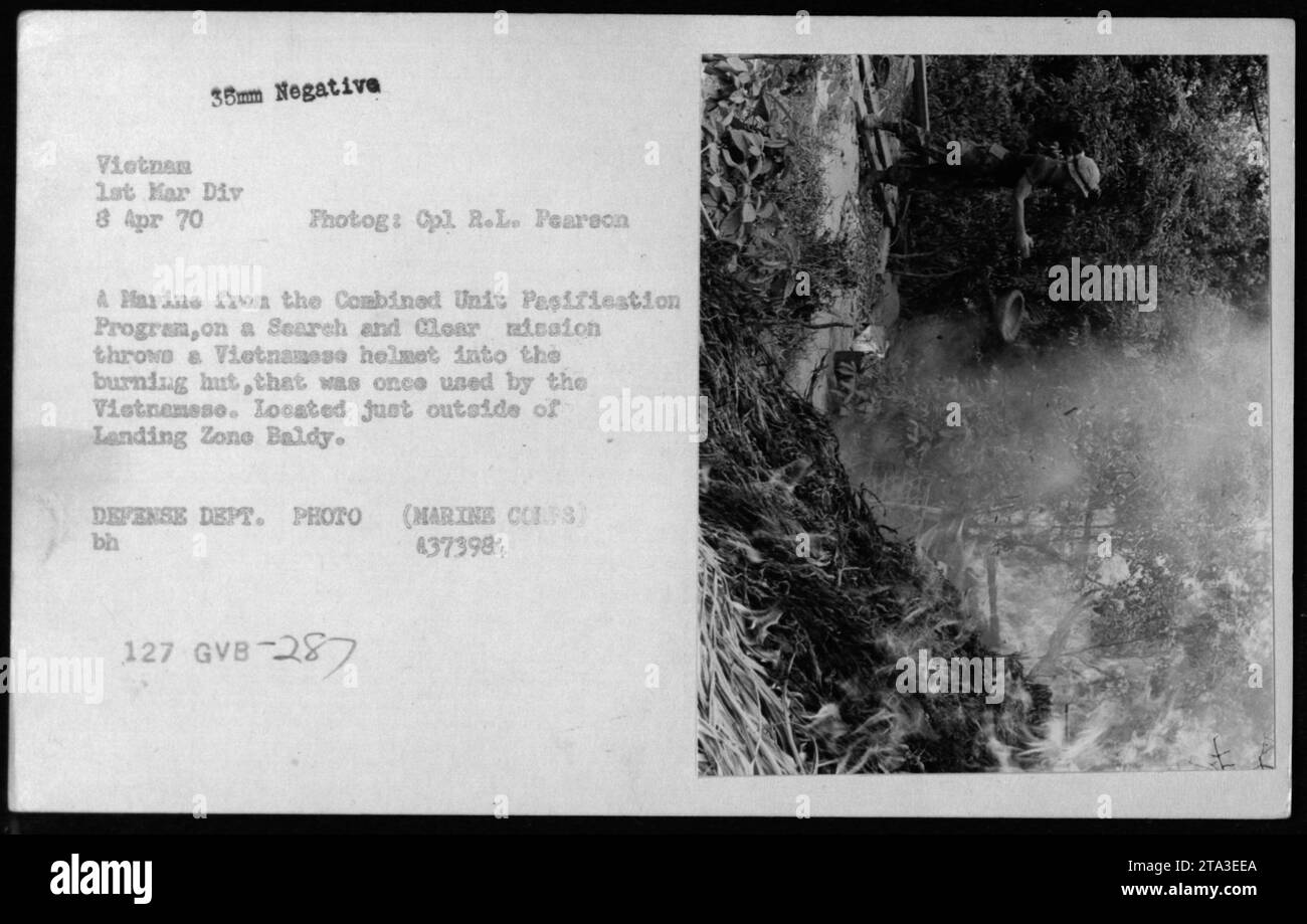 Un Marine du programme de pacification des unités combinées jette un casque vietnamien dans une hutte en feu lors d'une mission de recherche et de dégagement près de Landing zone Baldy, Vietnam, le 8 avril 1970. Cette photographie a été prise par le caporal R.L. Pearson dans le cadre des patrouilles de la 1e Division des Marines dans la région. Banque D'Images