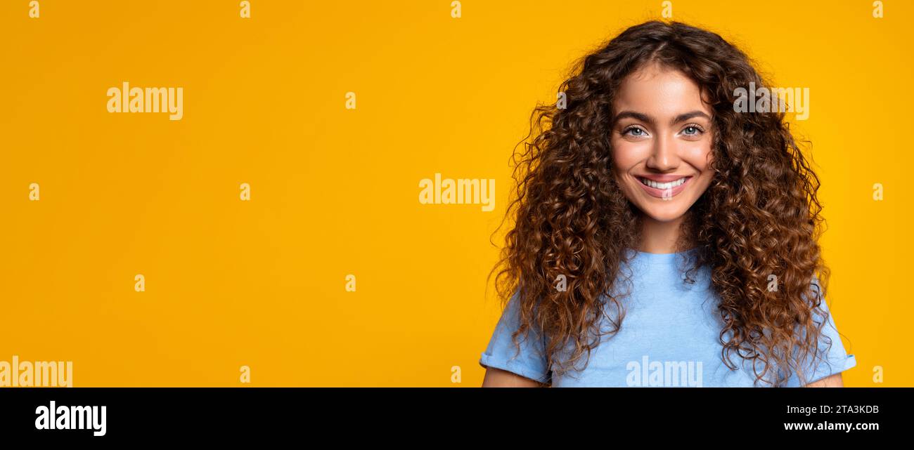 Femme aux cheveux bouclés souriante sur fond jaune, panorama, espace de copie Banque D'Images