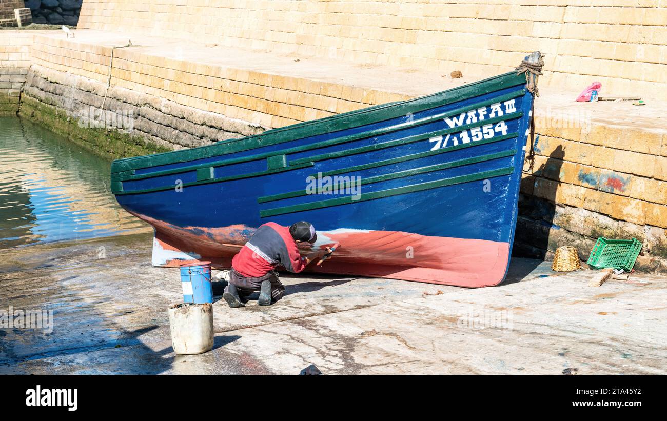 Essaouira, Maroc - 17 septembre 2022 : Homme peignant le traditionnel bateau de pêche bleu au port d'Essaouira Banque D'Images